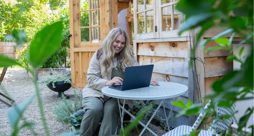 woman researching on laptop outside of green house