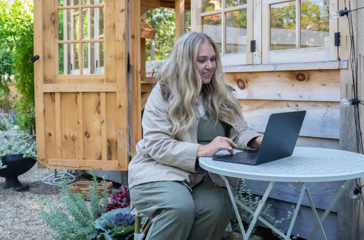 woman on laptop outside of green house